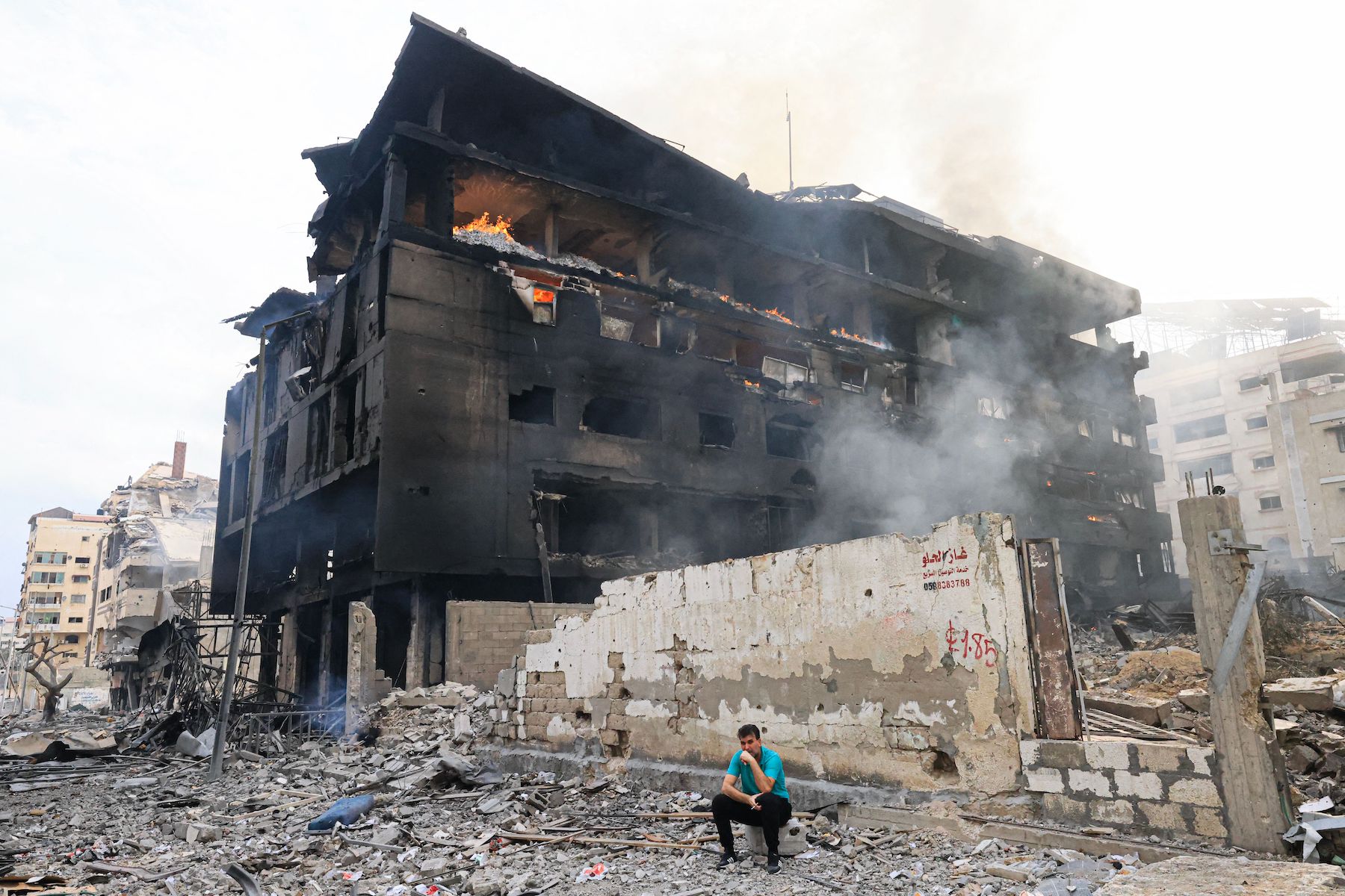 A Palestinian youth sits in front of a charred building