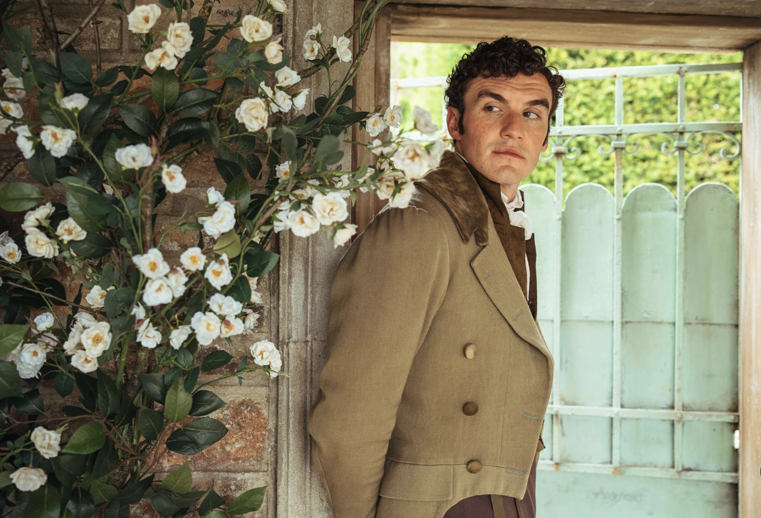 Tom Hayward (Dónal Finn) at the garden gate with a rosebush in bloom