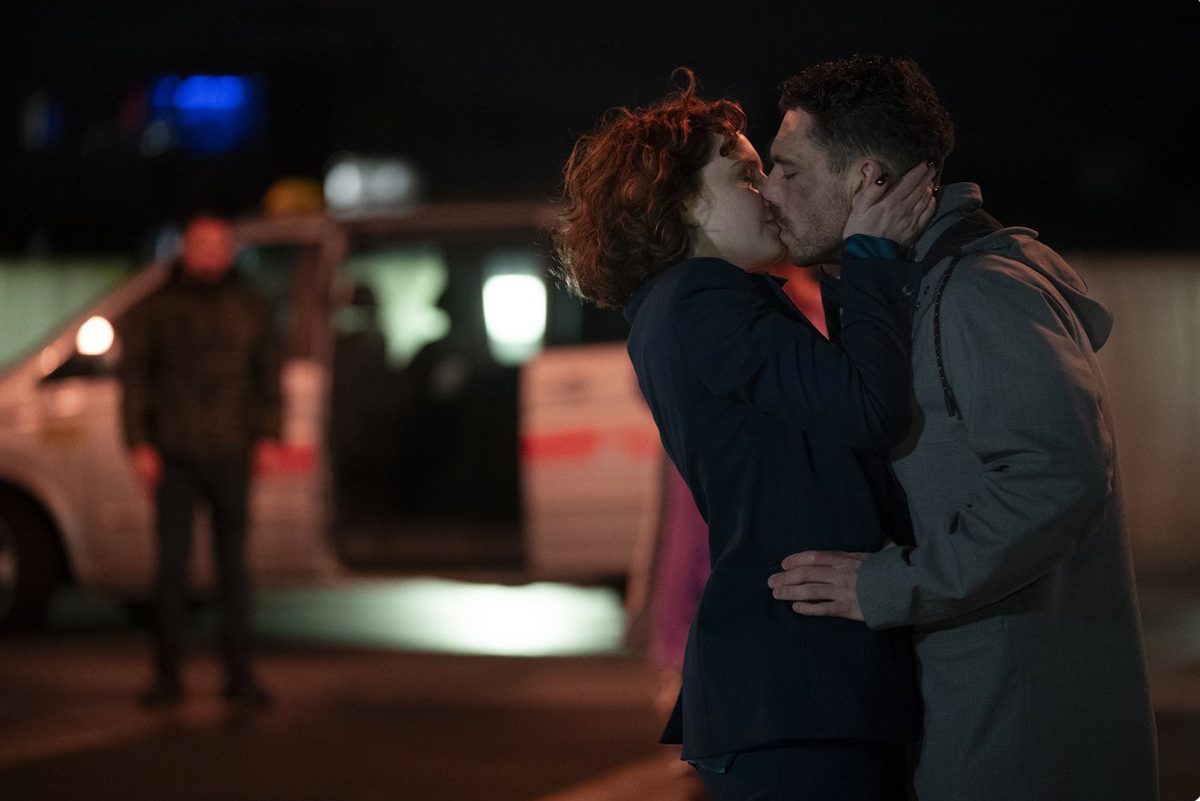 Michael (James Nelson-Joyce) and Diana (Hannah Onslow) exchange a passionate kiss while a car waits in the background