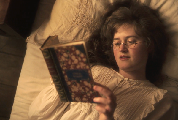 Mary Bennet (Ella Bruccoleri), hair loosened, wearing a nightgown, reads poetry in bed