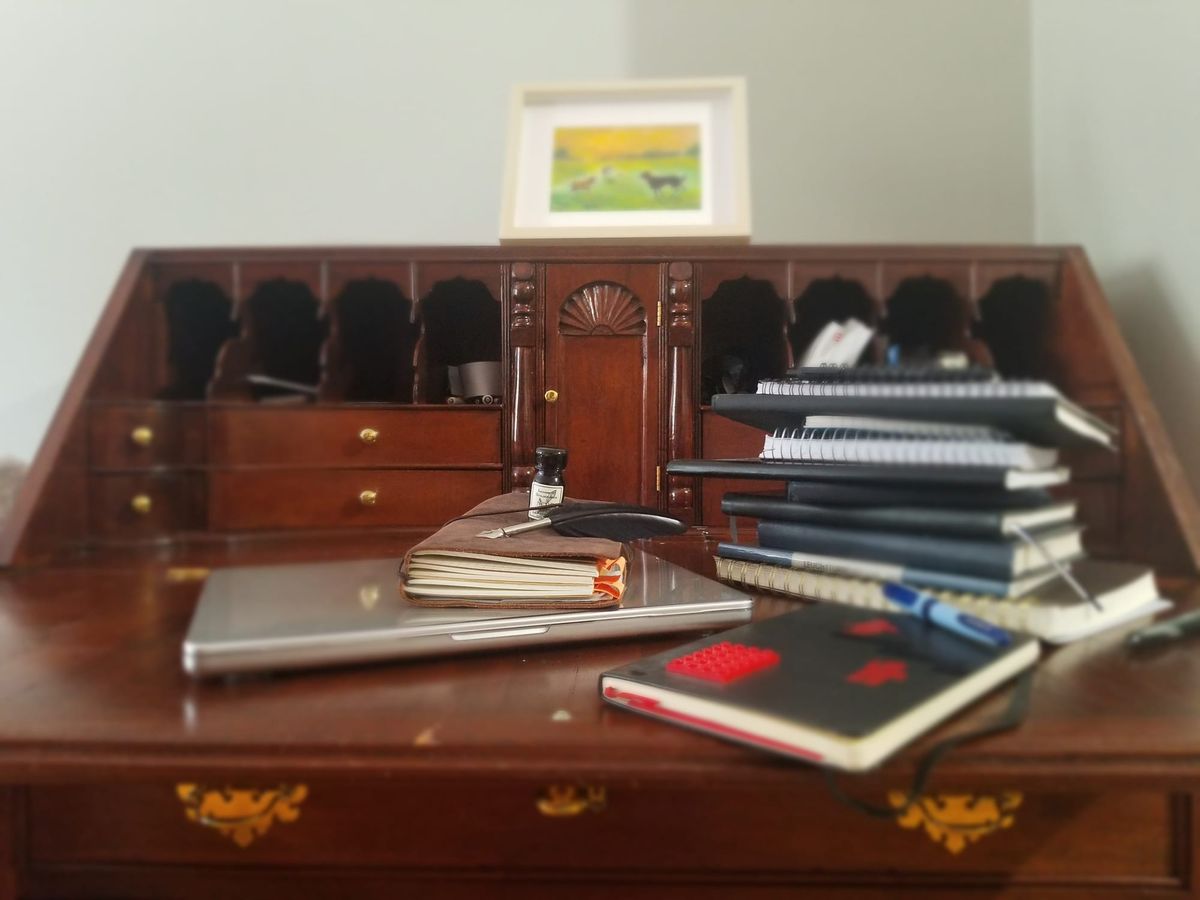 Desk with a laptop and a stack of filled notebooks, representing the Socratic Journal Method for building a lasting journaling habit.