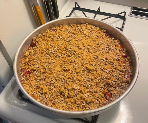 A berry crisp in a metal pan topped with sunflower seeds and streusel