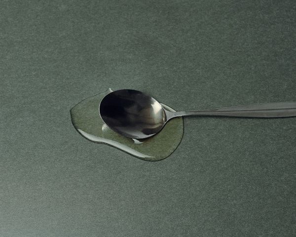A metal spoon full of syrup sits on a grey surface