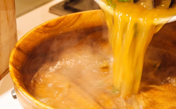 A photograph of steaming broth being ladled into a bowl
