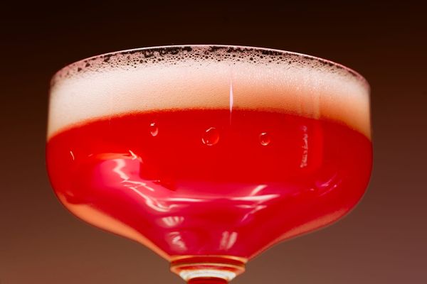 A coupe glass of a frothy red cocktail