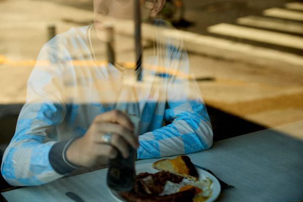 A view through a diner window of a person holding a glass soda bottle