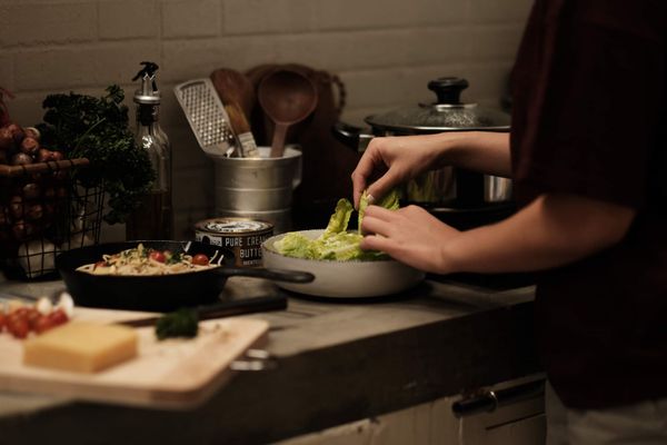 A person assembles a skillet of spaghetti and a bowl of salad on a kitchen counter