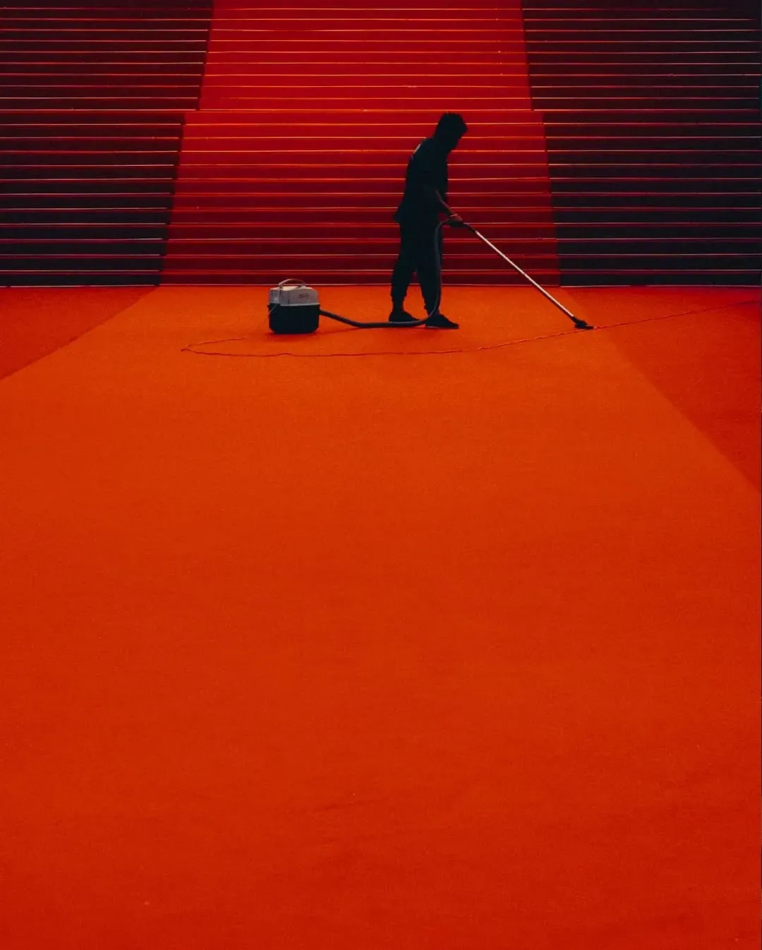 A person vacuums a red carpet at the foot of a staircase: cleaning up after the show
