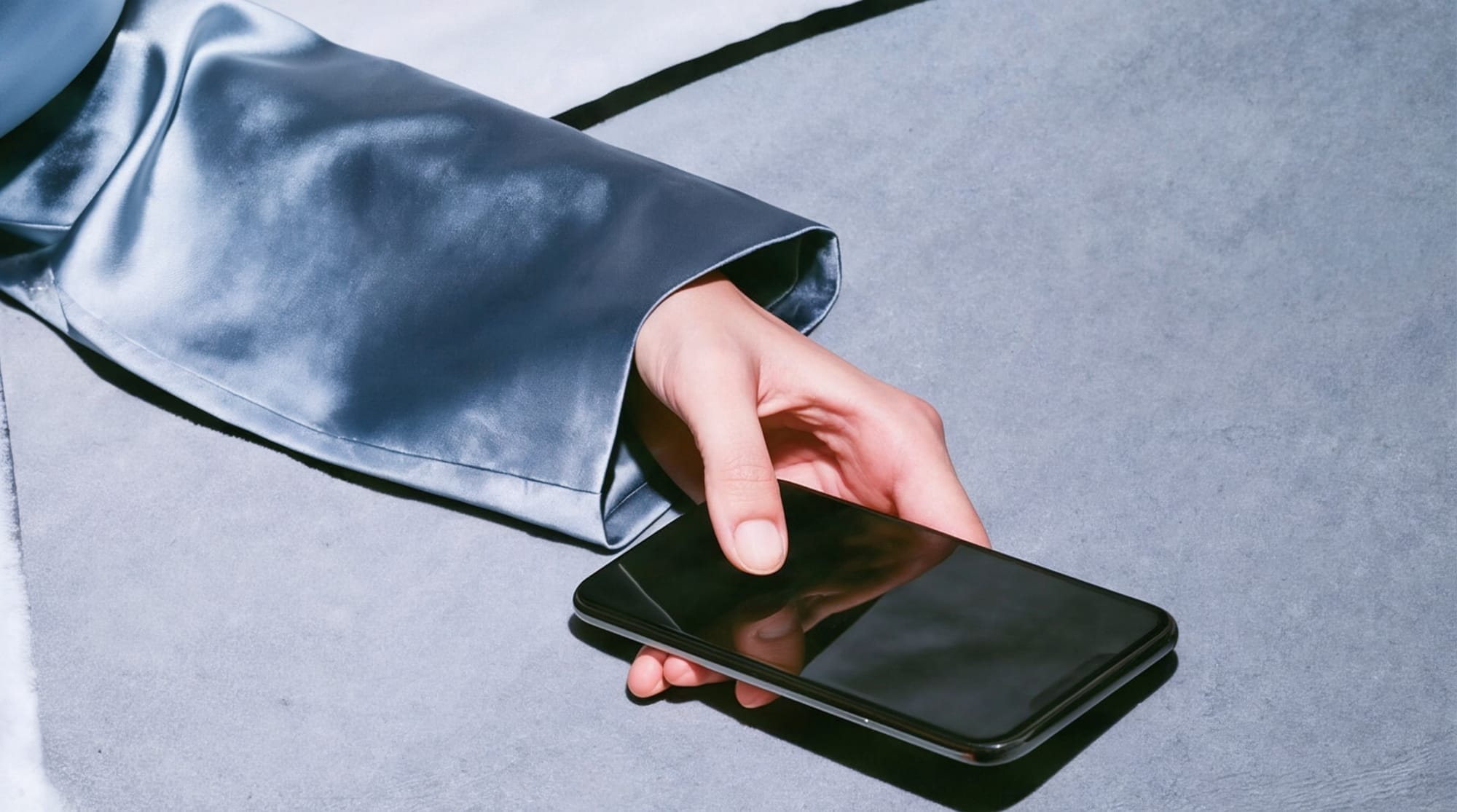 Hand resting on a smartphone, blue satin sleeve
