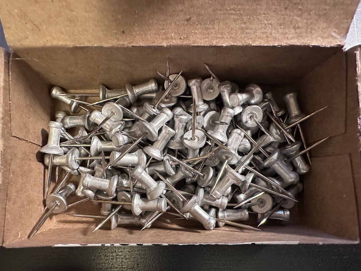silver pushpins in a cardpaper box that have a long spiky point.