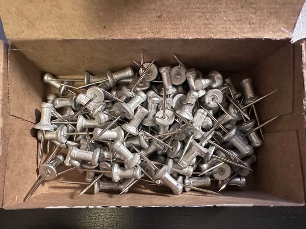 silver pushpins in a cardpaper box that have a long spiky point.