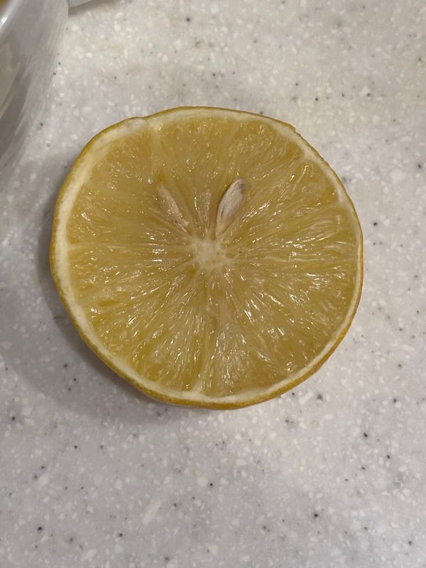 Half a small yellow bergamot fruit with two seeds prominent, sat on a white, grey & black speckled kitchen counter.