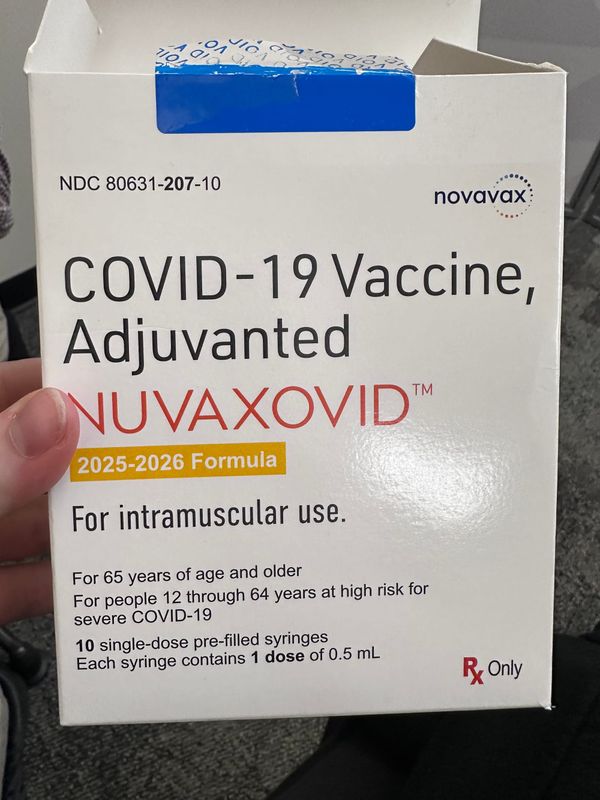 White person’s hand holding up an open box for Nuvaxovid Covid-19 Vaccine.