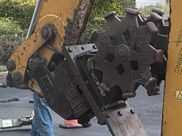 Some sort of huge grinding digger wheels on a hydraulic arm with debris in the background.