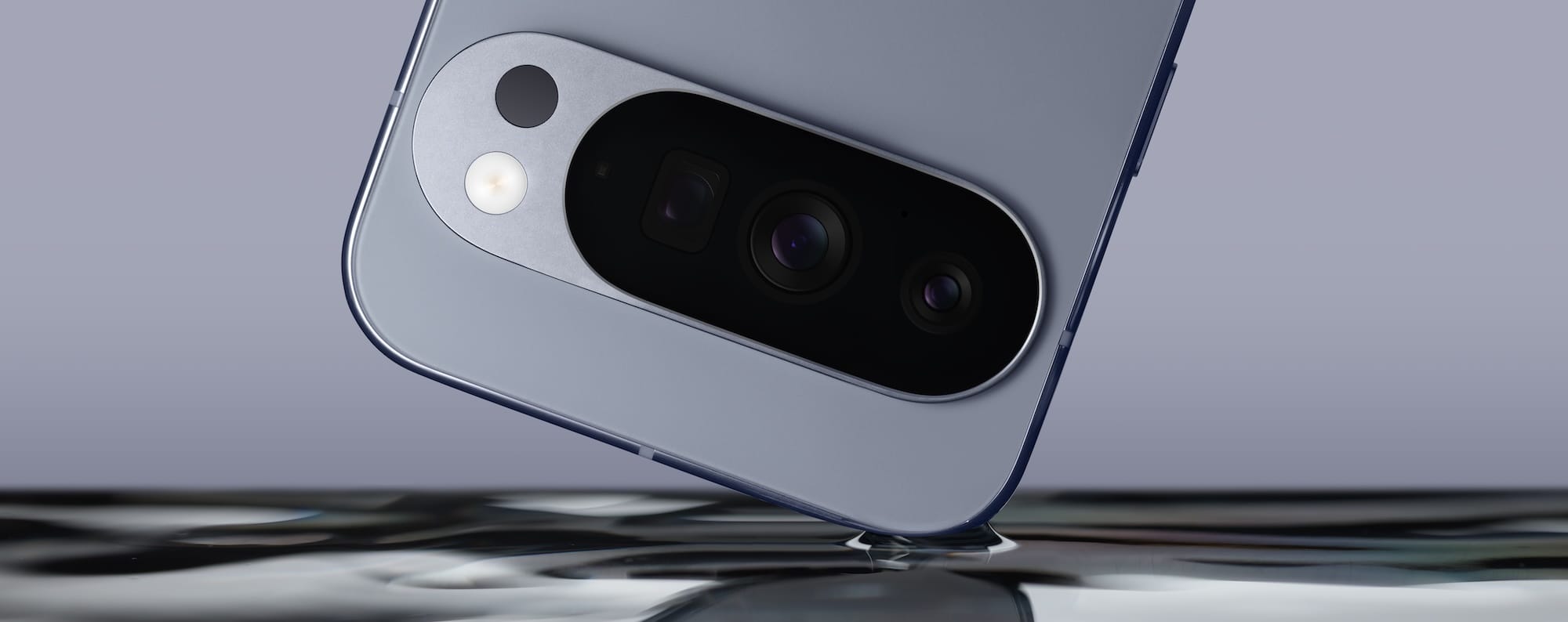 An upside-down Pixel 10 Pro top section with a corner touching a water surface. Grey phone and grey background.