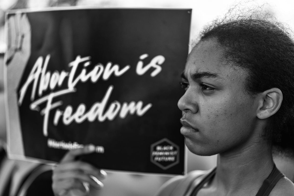 Black and white photo of young Black woman holding up a sign that reads "Abortion is Freedom."