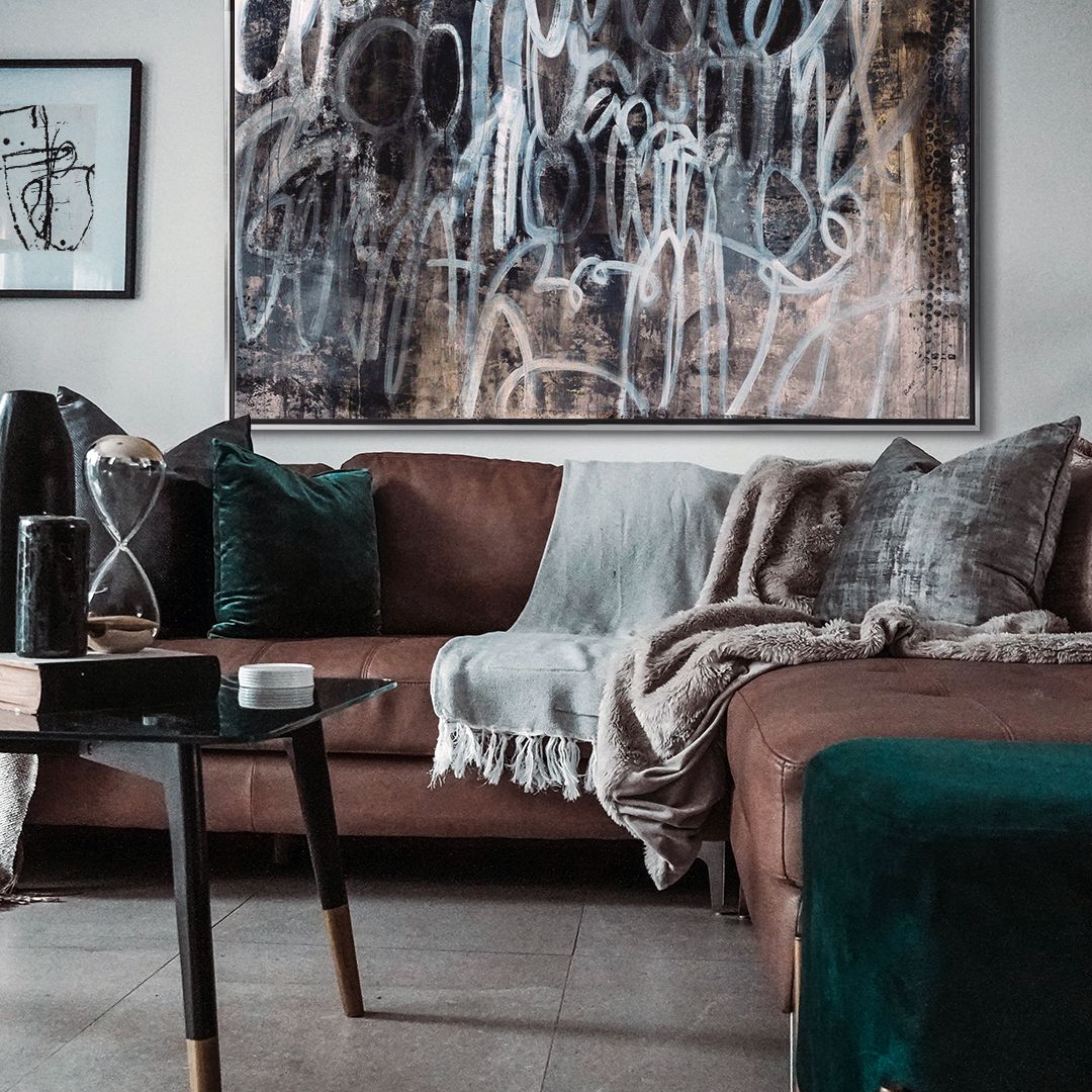 Large contemporary abstract print in silver floating frame over a cozy couch in neutral living room.
