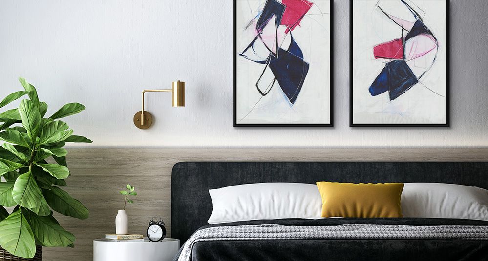 Two symmetrical abstract art prints in black floating frames over the headboard of a bed.