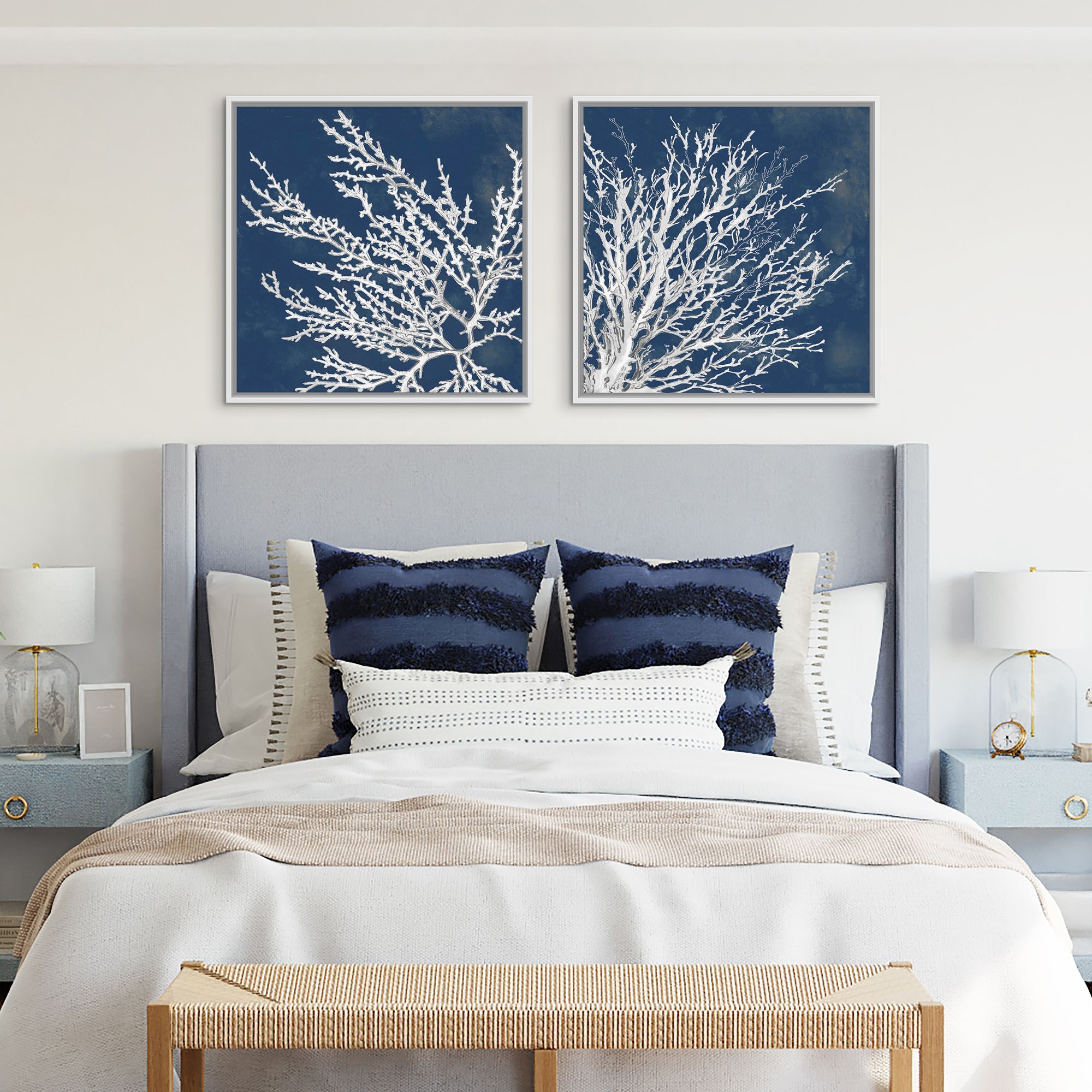 Two coastal art prints in white floating frames over a headboard in a coastal bedroom.