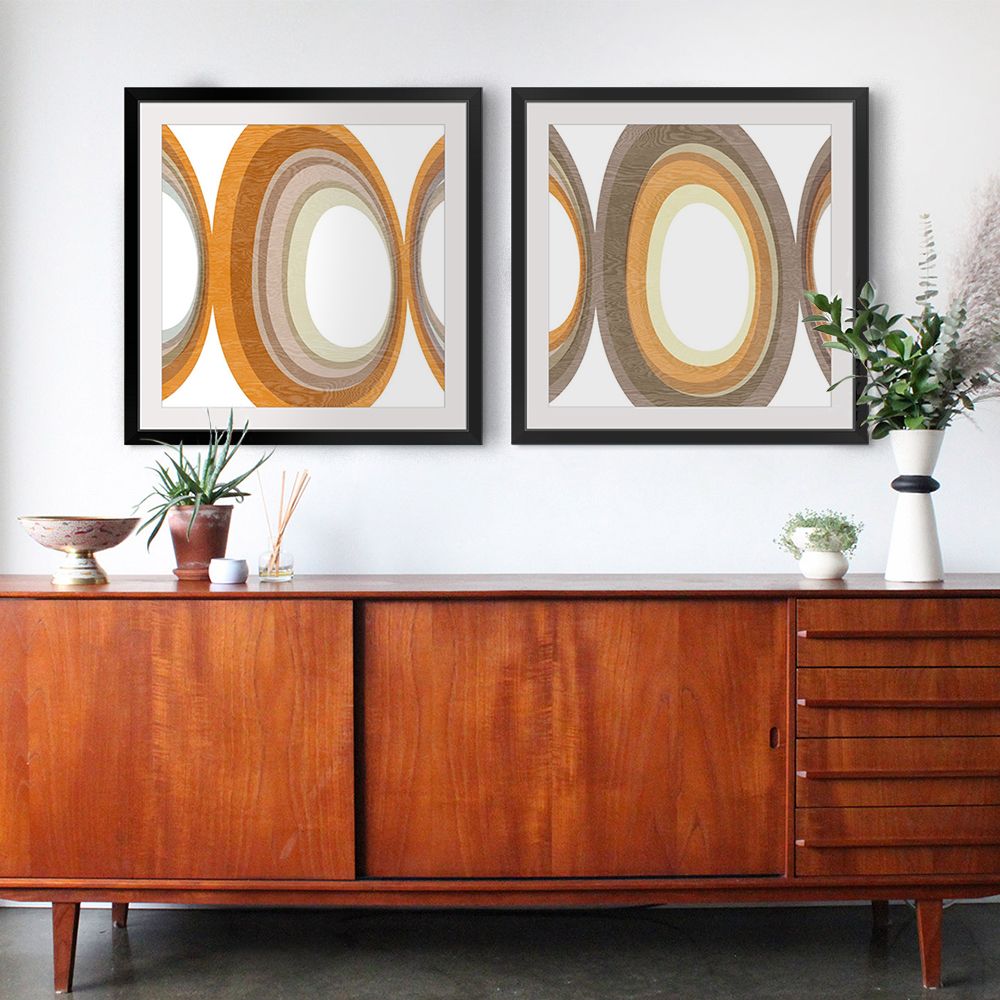 Two geometric, warm-toned wall art designs in brown frames over a brown dresser with plants.