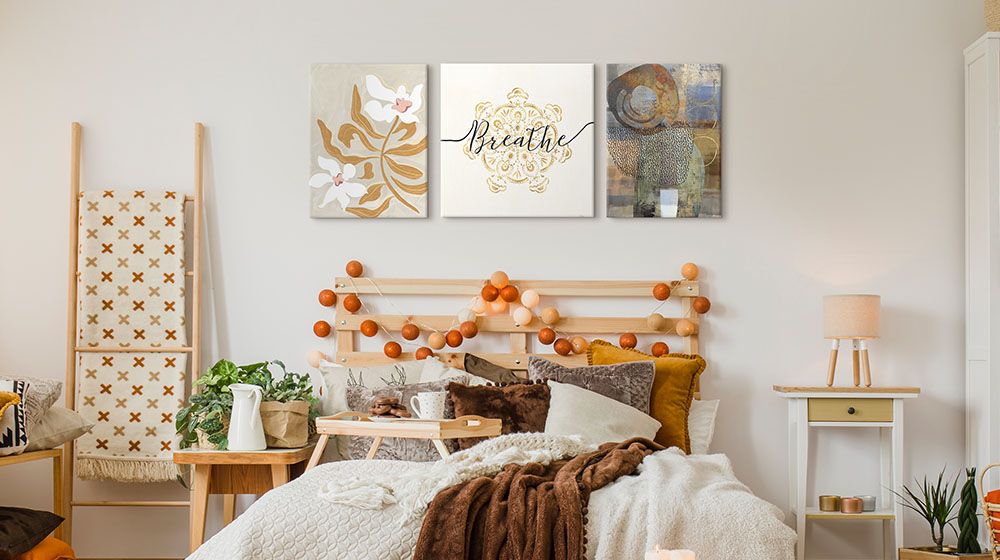 Three pieces of art hung side-by-side over a bed in a bohemian room. "Flower Flower Flower" by Arty Guava, "Namaste II" by Veronique Charron & "Tipping Point" by Nikki Chu