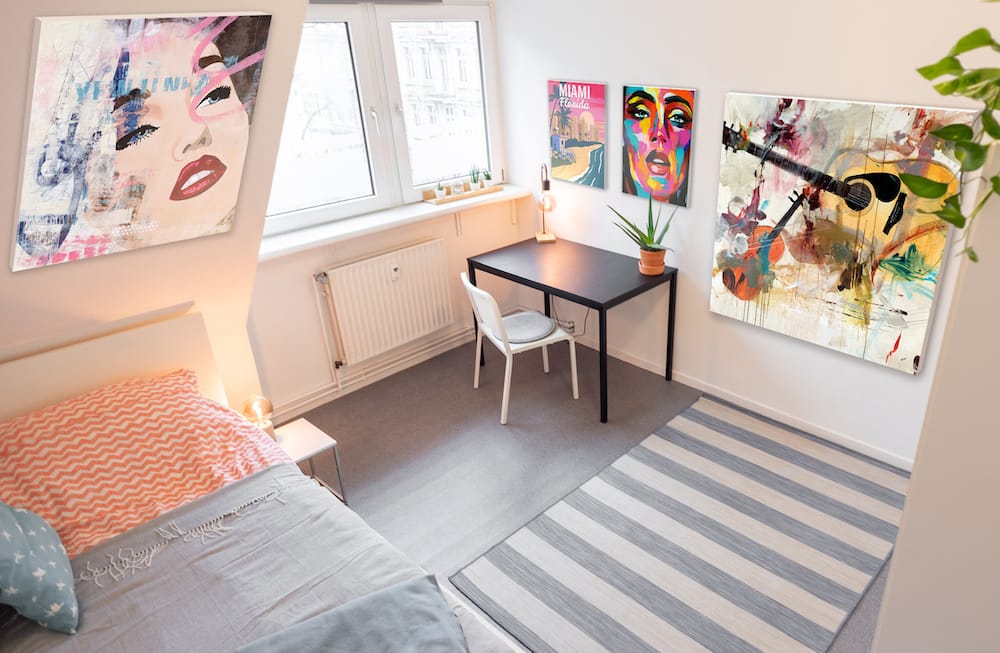A cozy and decorated college dorm room with multiple colorful art works hung on wall