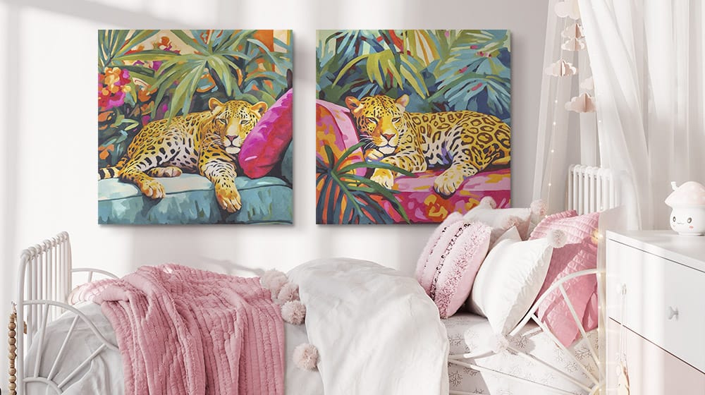 Two bright leopard art canvas prints on the wall in a soft pink and white children's bedroom