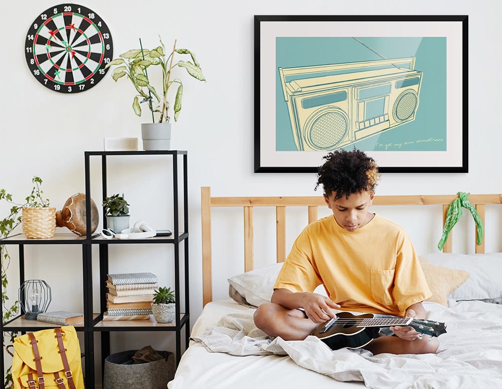 Young boy sitting on a bed in their room with a graphic framed print of a radio on the wall behind them