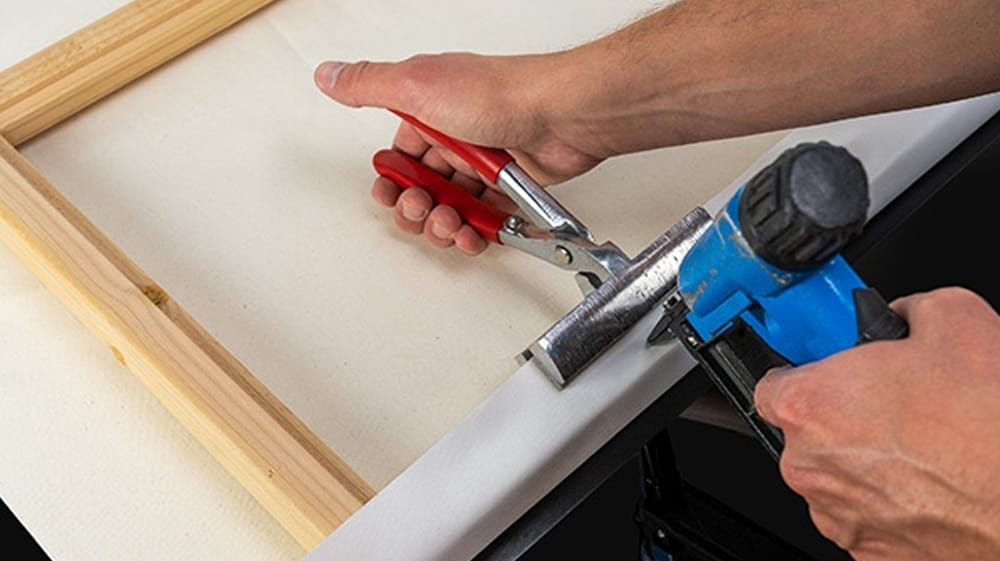 Artisan stretching canvas by hand over a solid wood stretcher frame during production