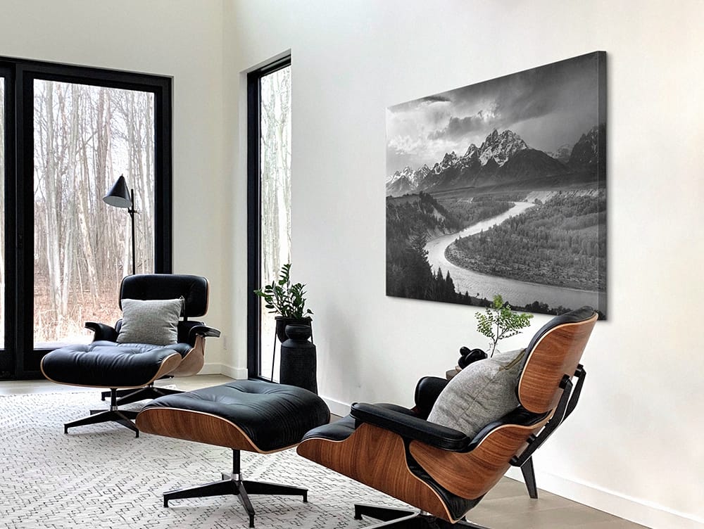 Large black and white landscape canvas print displayed in a modern living room with lounge chairs