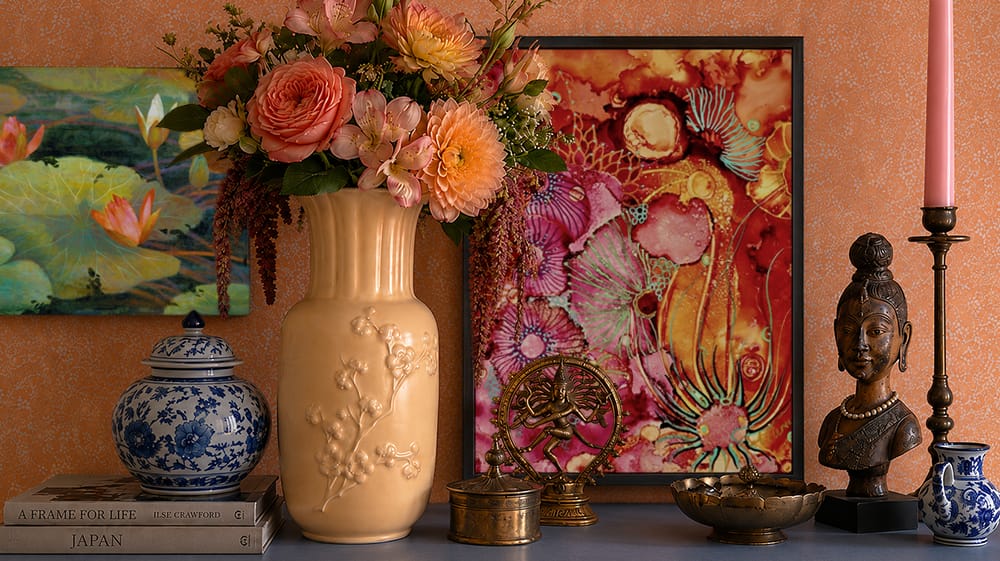 Global maximalist vignette layering colorful wall art with florals, blue-and-white ceramics, sculptural decor and warm tones.