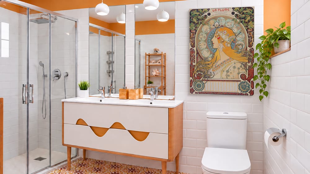 Decorative canvas wall art hangs beside the vanity in a bright modern bathroom with white tile and warm orange accents.