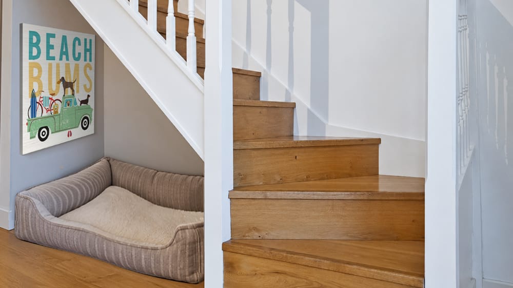 Colorful canvas wall art hangs beneath a staircase above a dog bed, adding personality to the small wall space tucked under the stairs.