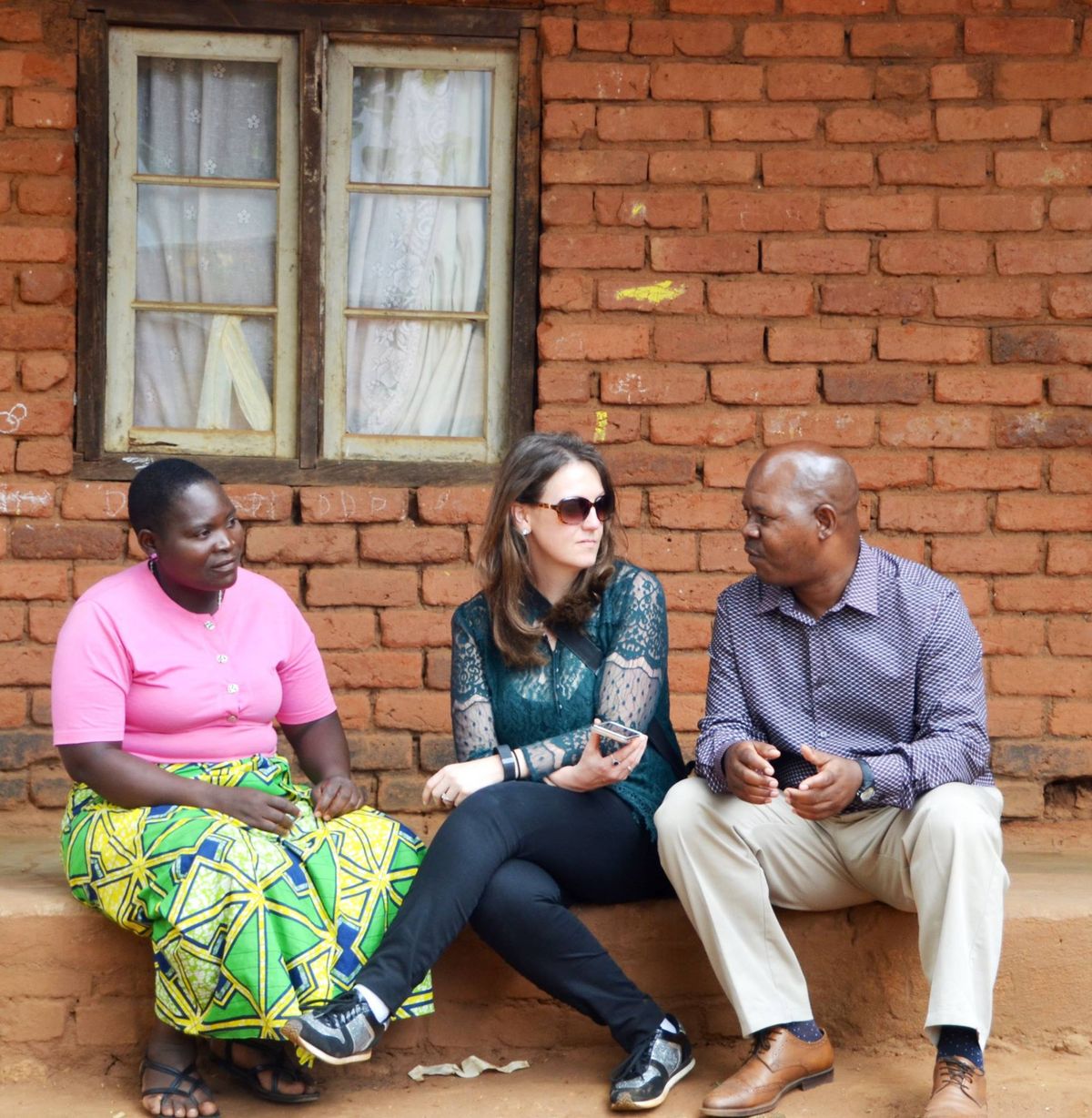 Three people sit along a curb, talking with one another. 