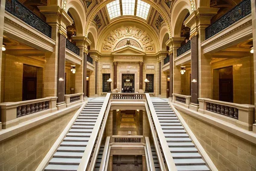 Two, side-by-side staircases leaded up to an ornate doorway, flanked on either side by hallways lined with tall columns.