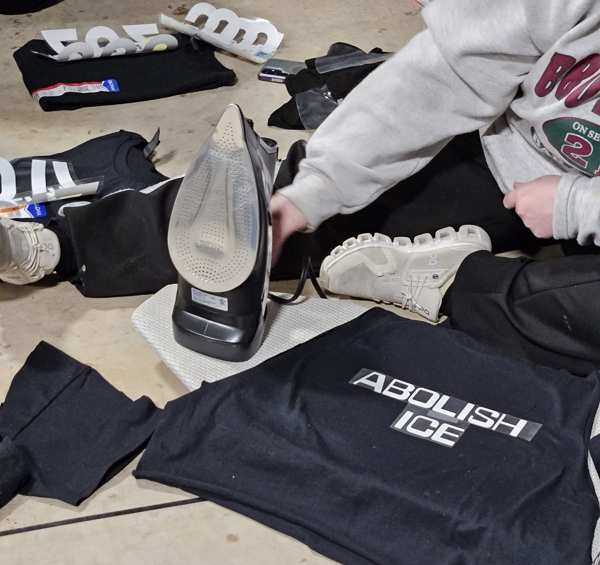 Close-up shot of a person using a hot iron to put text on a black t-shirt. The text reads, "Abolish ICE."