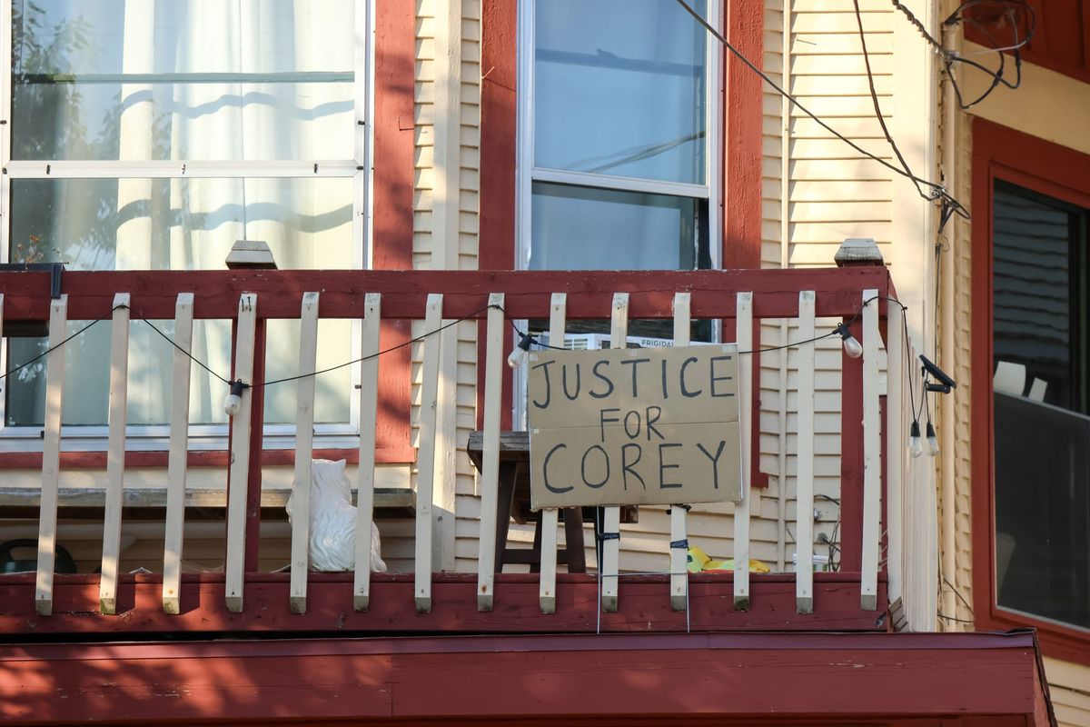 A cardboard sign hanging from a balcony reads "Justice for Corey"