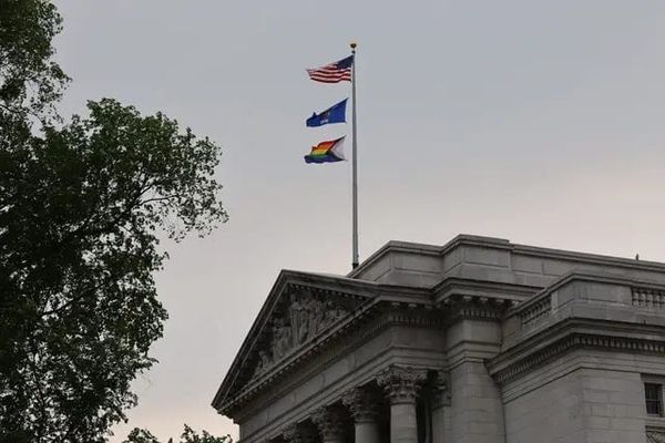 The Progress Pride flag flies underneath the Wisconsin and U.S. flags on a pole over top of the ornate facade of WI State Capitol building.