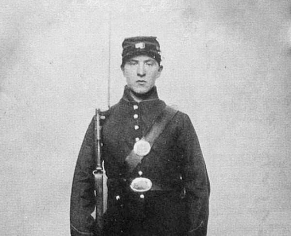 An old black and white photo shows a solder dressed in a Union Civil War uniform, with a musket on his shoulder.