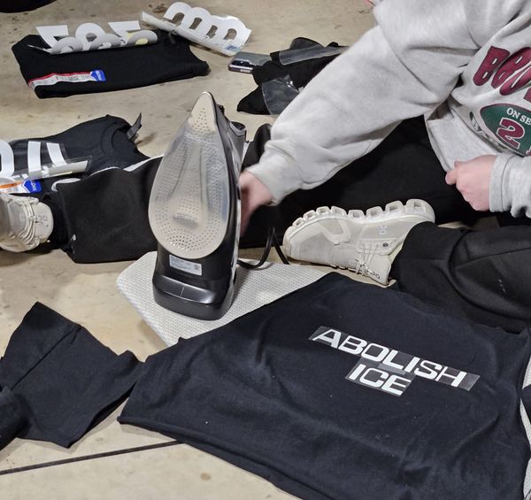 Close-up shot of a person using a hot iron to put text on a black t-shirt. The text reads, "Abolish ICE."