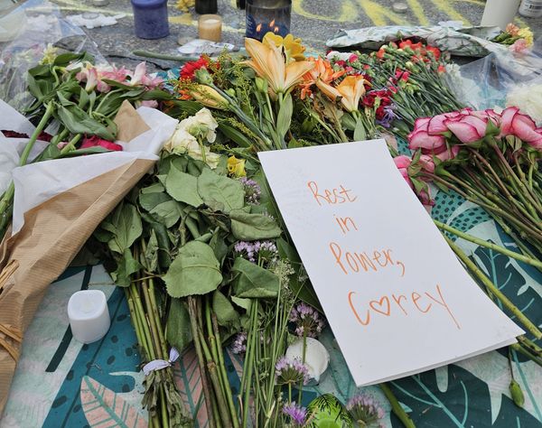 A bundle of flowers lays on the ground. A card with "Rest in power, Corey" written on it lays on top.
