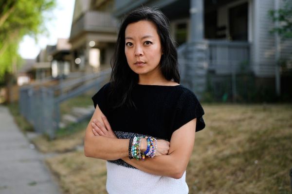 Francesca Hong, a middle-aged woman with long black hair, stands with crossed arms and wearing multiple friendship bracelets. 