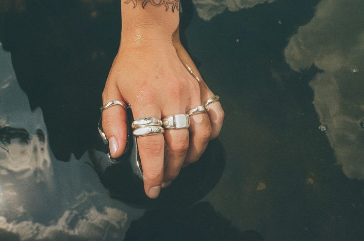 Human hand wearing silver rings on each finger, waving in a pool of water.