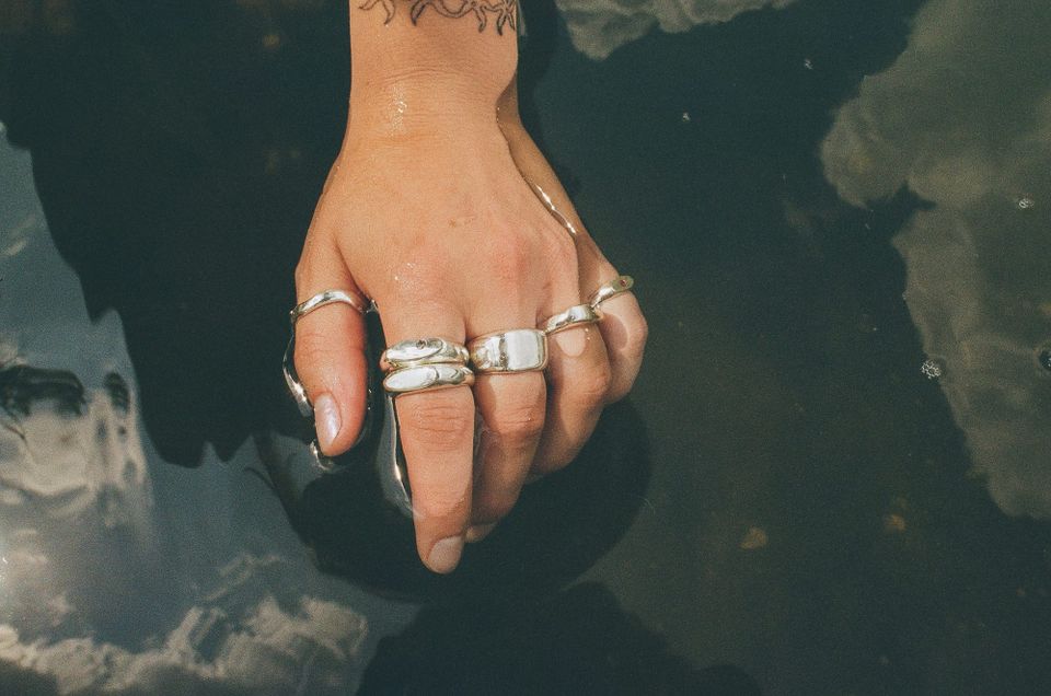 Human hand wearing silver rings on each finger, waving in a pool of water.
