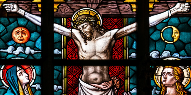 A colorful stained glass window in six panels featuring Jesus on the cross, Mary Mother of Jesus gazing up at her son, another haloed figure, and a sad-looking sun and moon.