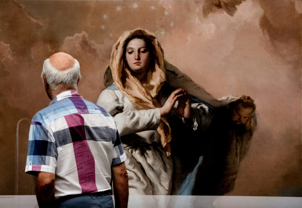 We see the back of the head of a man as he walks by a painting of Mary, Queen of Heaven with a halo of stars circling her head. She seems to meet the man's gaze.