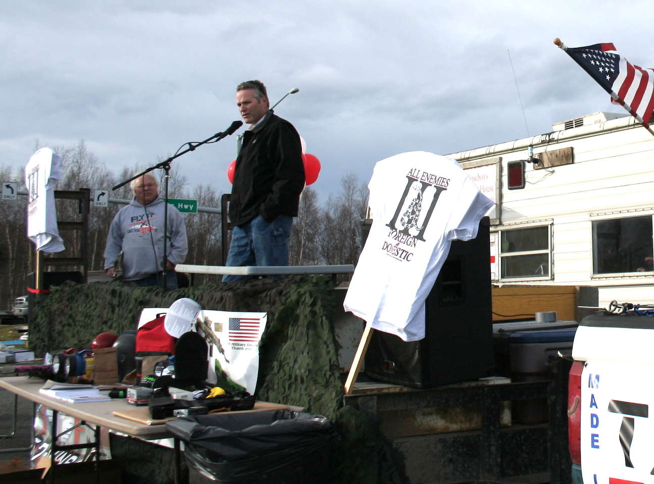 Alaska Governor Mike Dunleavy speaks at a public event where "all enemies foreign and donestic" were emblazoned on t-shirts.
