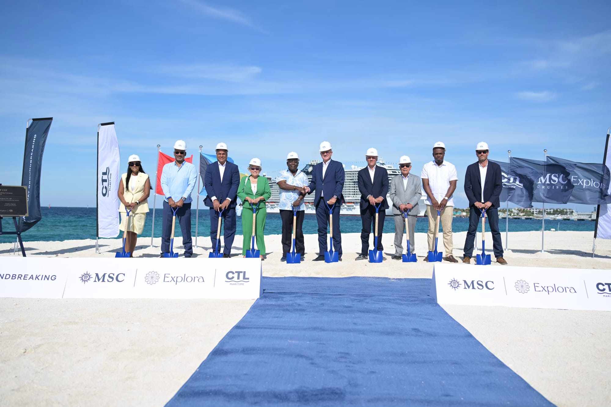A group of officials in hard hats poses with blue shovels on a beach during the Sandy Cay groundbreaking ceremony.