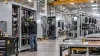 Workers assemble electrical power-distribution cabinets and cooling frames on a modern data-center infrastructure factory floor.