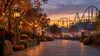 Generic amusement park walkway decorated for fall at dusk with a roller coaster silhouette